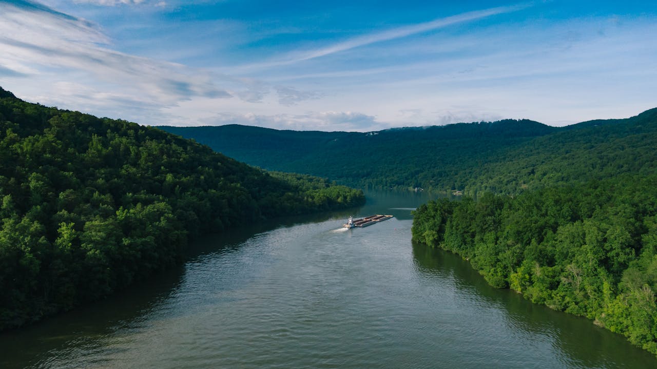 Breathtaking aerial view of a barge navigating a winding river amid lush green mountains.